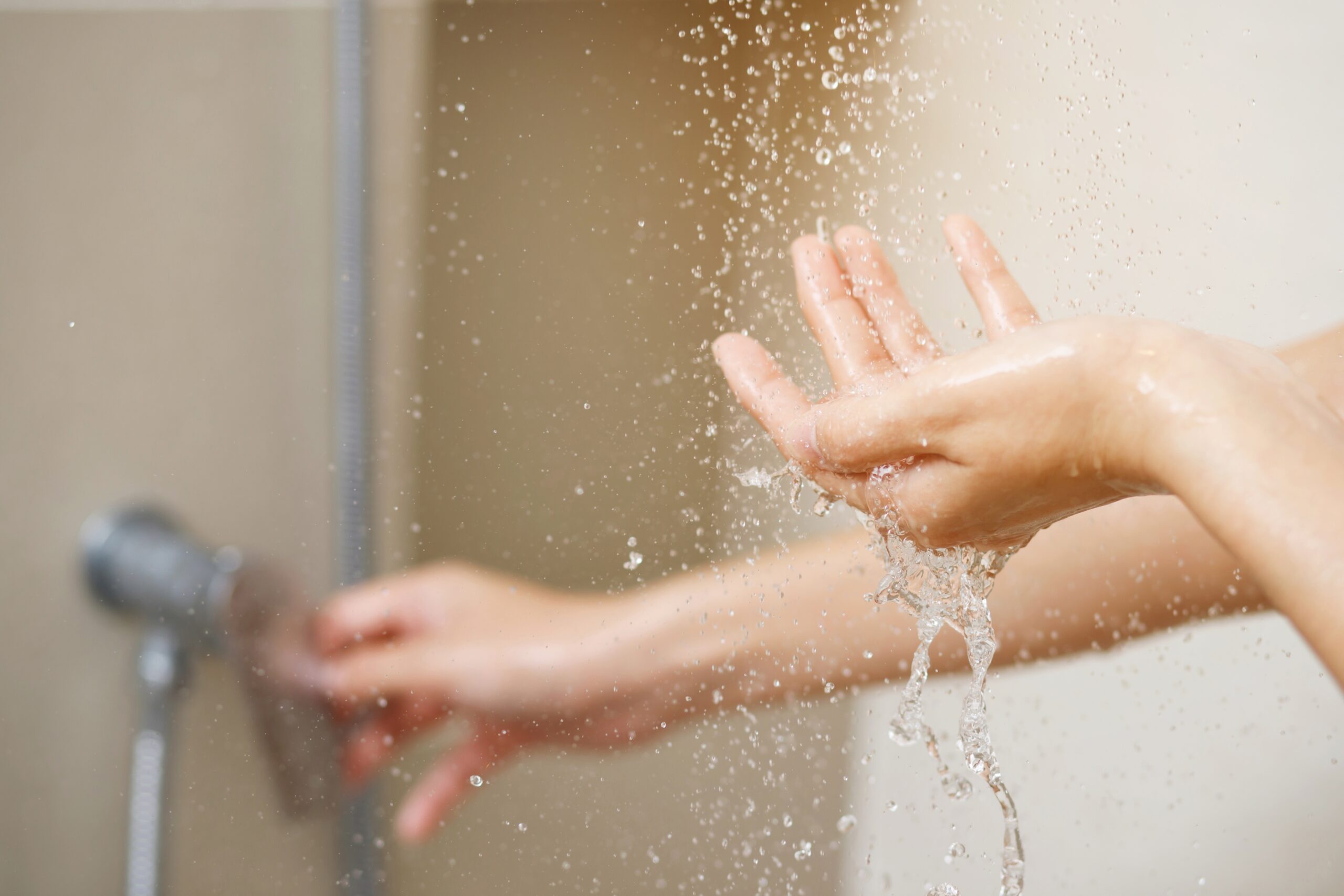 A person tests the temperature of running shower water with one hand while adjusting the water control with the other.