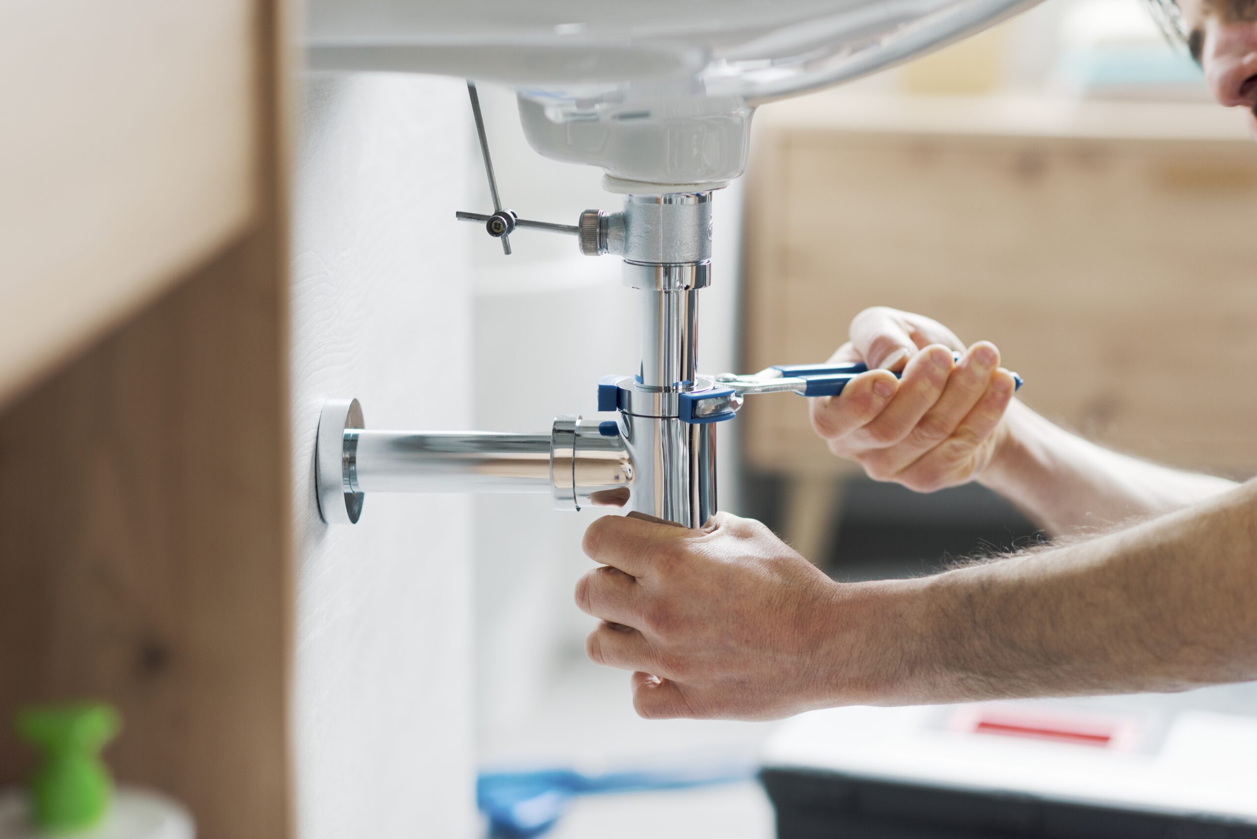 A person using a wrench to tighten the plumbing connections under a bathroom sink.