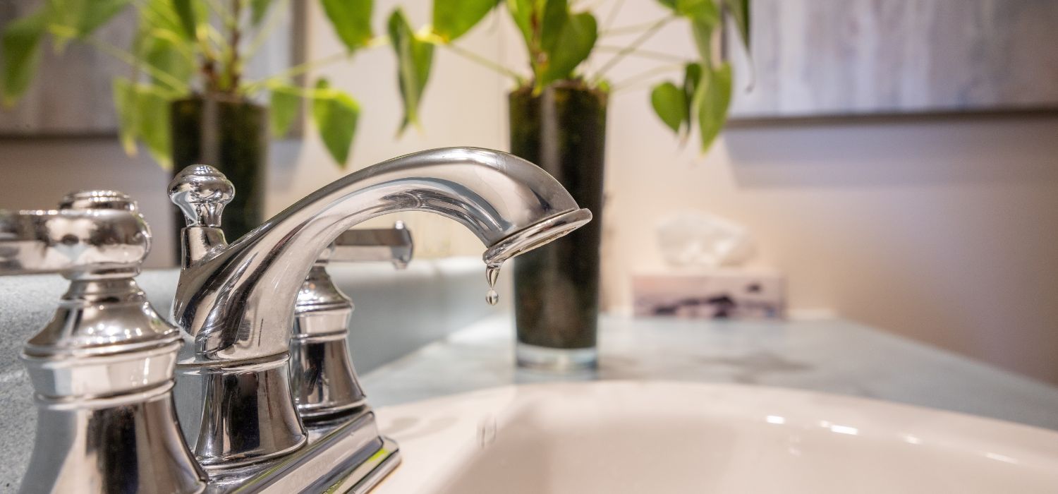 A close-up of a bathroom faucet dripping water into the sink, representing a plumbing leak that could be found during a plumbing inspection.