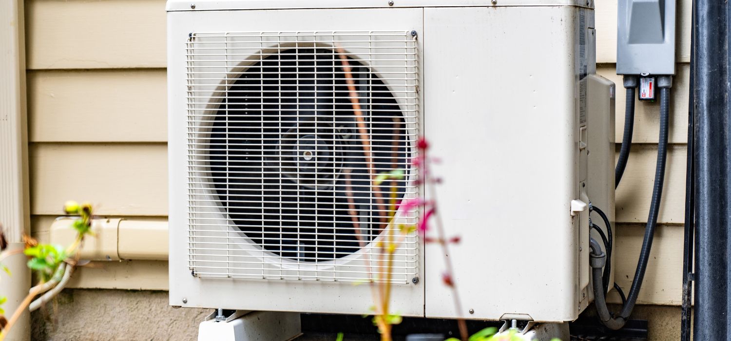 Outdoor air conditioning condenser unit installed beside a home, showing the fan, electrical connections, and housing typical of residential HVAC systems.